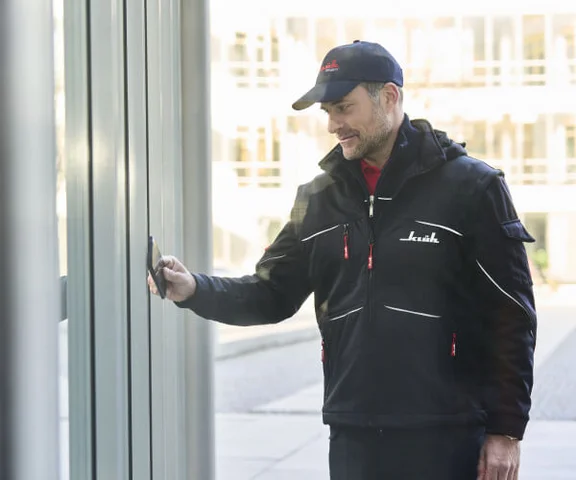 Ein Sicherheitsmitarbeiter in Berufskleidung verschafft sich mithilfe einer Magnetkarte den Zugang zu einem Gebäude.