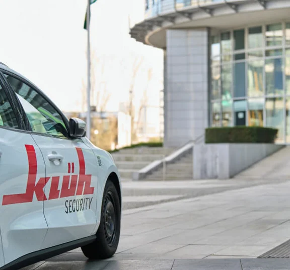 Das Bild zeigt ein weißes Auto mit Klüh-Logo, das vor einem Gebäude hält.