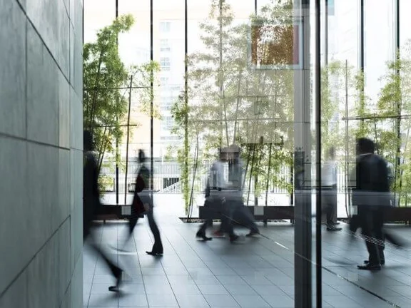 Ein Bild von einem Flur einem Gebäude mit einer Glasfassade, einige Menschen gehen den Flur entlang