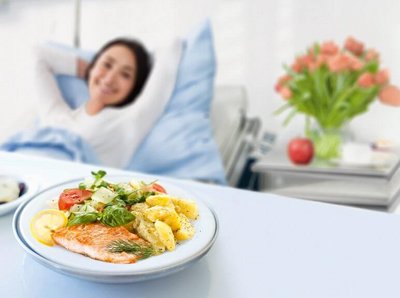Weibliche Person liegt im Krankenbett und sieht lächelnd auf ihr Essen.