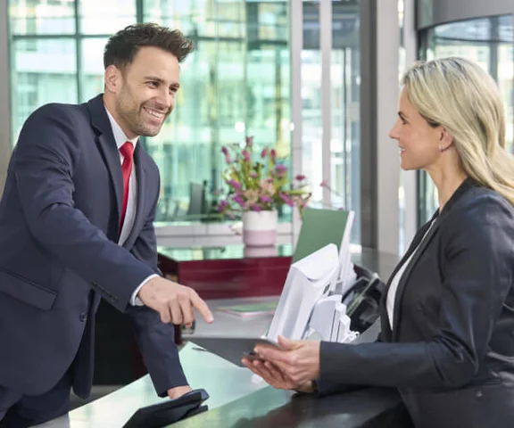 Eine männliche Empfangskraft ist im Gespräch mit einer weiblichen Besucherin.