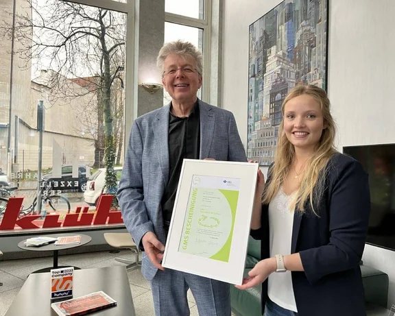 Ein Bild von einem Mann und einer Frau die zusammen eine GMS Bescheiniung halten ausgestellt in der Klüh Hauptverwaltung in Düsseldorf