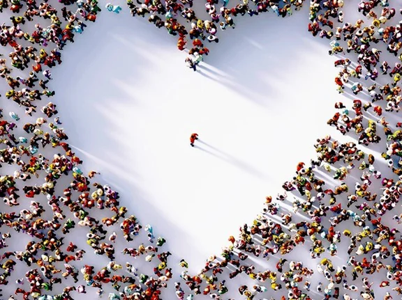 Ein Bild von sehr vielen Menschen die stehen aus der Vogelperspektive, die so stehen das eine fläche freisteht und ein Herz bildet, in der mitte des Herzes steht nur 1 Mensch