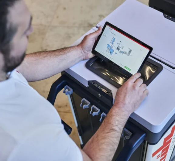 Klüh Reinigungskraft stehend an seinem Reinigungswagen bedient ein Tablet