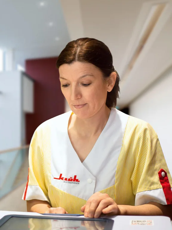 Eine weibliche Reinigungskraft von Klüh sieht auf ein Ipad, um zu sehen, welche Räume noch gereinigt werden müssen.